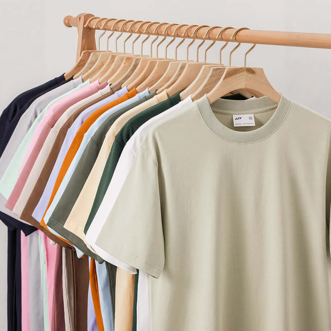 Xinjiang cotton heavyweight t-shirt en varios colores colgados en un perchero de madera.
