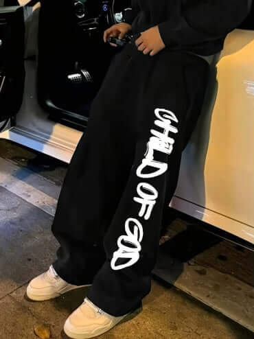 Pantalones holgados streetwear para hombres en color negro, con estampado 'CHILD OF GOD' en el lado.